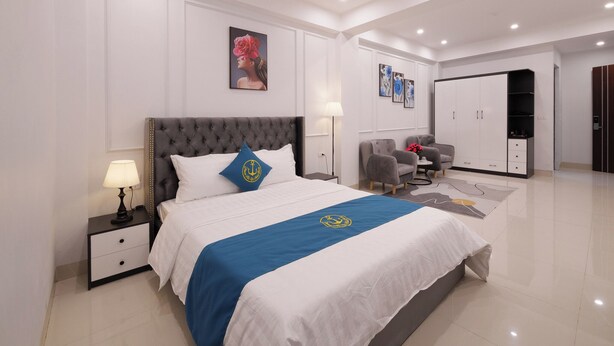 A modern hotel room with a large bed, bedside lamps, a wardrobe, and a seating area with armchairs. - RUBY 2 HOTEL (Hanoi)
