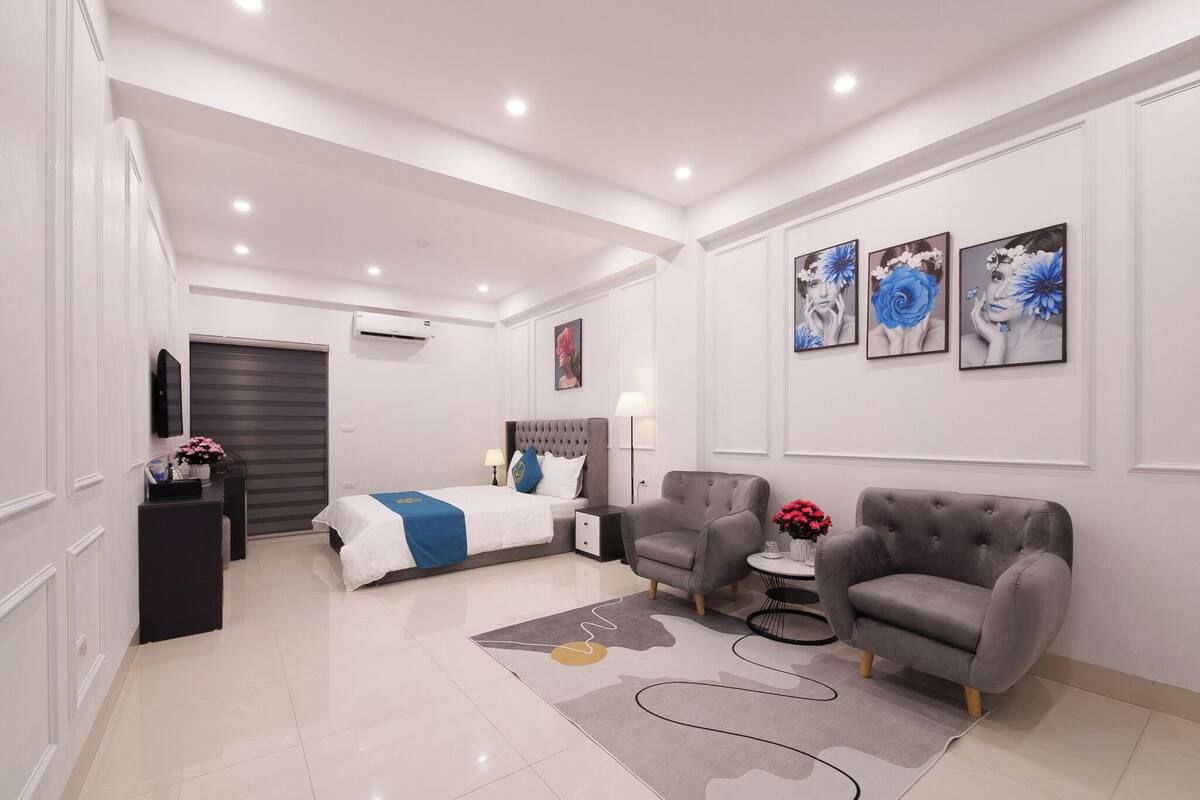 Quarto de hotel moderno com cama, duas poltronas, mesa lateral, escrivaninha, televisão de tela plana e obras de arte nas paredes.