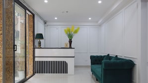 A reception area with a white reception desk, a green sofa, and a potted plant. - RUBY 2 HOTEL (Hanoi)