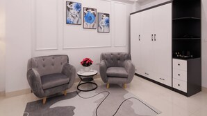 A modern living room with two grey armchairs, a small round table with a vase of flowers, and a large black and white wardrobe. - RUBY 2 HOTEL (Hanoi)