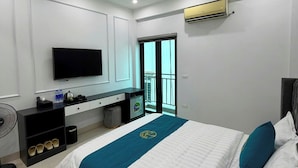 A hotel room with a bed, a TV, a minibar, a fan, and an air conditioning unit. - RUBY 2 HOTEL (Hanoi)