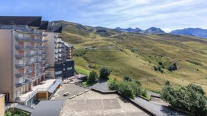 A multi-story building with balconies, a parking area, and a view of rolling hills and mountains. - Central Auris-en-Oisans Stay for 4 (Germ)