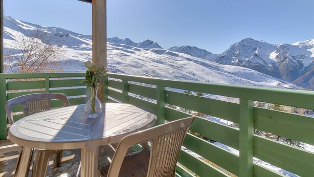 A table with chairs on a balcony with a mountain view. - Central Auris-en-Oisans Stay for 4 (Germ)