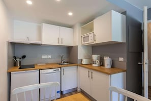 Eine kompakte Küche mit weißen Schränken, einer Mikrowelle, einer Kaffeemaschine, einem Geschirrspüler und einem kleinen Kühlschrank.