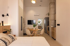 A modern hotel room with a bed, bedside table, lamp, and a view into the dining area. - Almirante Suites B (València)