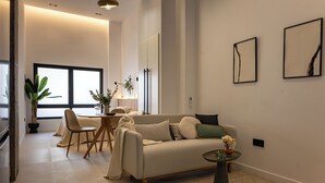 Ein modernes Wohnzimmer mit einer Couch, Sesseln, einem Esstisch und einem großen Fenster.