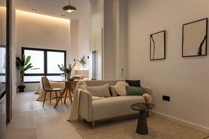 A modern living room with a sofa, chairs, a dining table, and a large window. - Almirante Suites B (València)