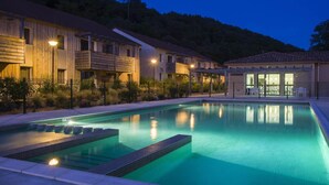 A swimming pool with steps, a covered seating area, and a building with balconies. - Stay in Les Eyzies with Pool (LES  EYZIES  DE  TAYAC)