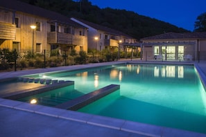 Ein Schwimmbecken mit Stufen, einem überdachten Sitzbereich und einem Gebäude mit Balkonen.