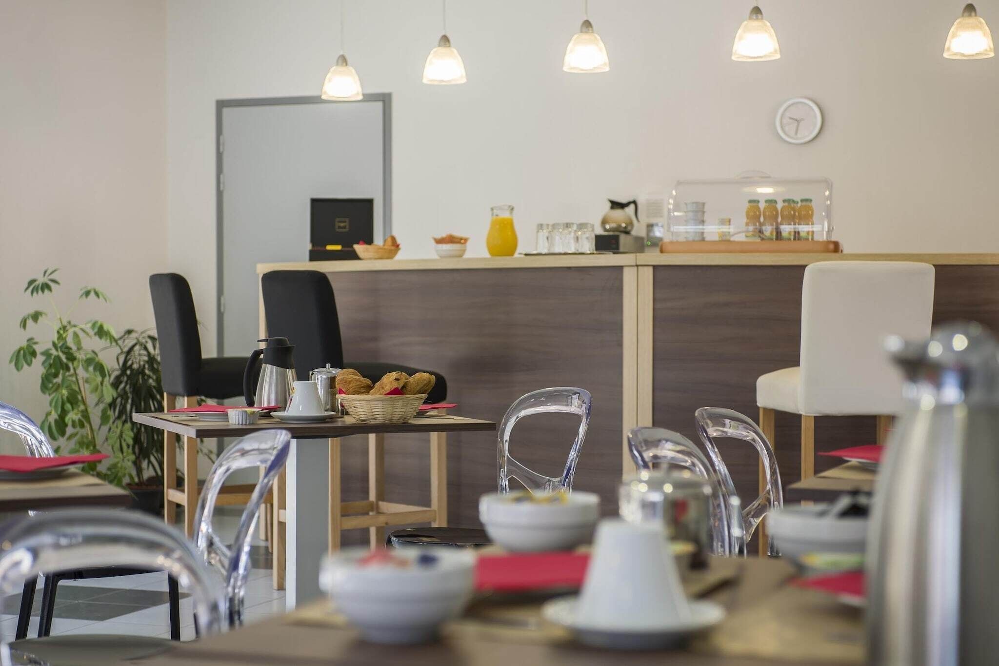 L’intérieur d’un café moderne, avec un comptoir en bois, des chaises transparentes et des lampes suspendues.