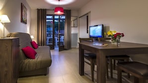 A room with a sofa, a dining table, a TV, and a vase with flowers. - Stay in Les Eyzies with Pool (LES  EYZIES  DE  TAYAC)