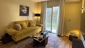 A living room with a sofa, coffee table, and a painting on the wall. - Luxury Stay in Sheikh Zayed -Private Garden + Swimming Pool (6th of October City)