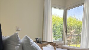 A bedroom with a bed, a bedside table, a window with curtains, and a view of greenery outside. - Luxury Stay in Sheikh Zayed -Private Garden + Swimming Pool (6th of October City)