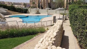 A swimming pool with a stone wall and a paved walkway. - Luxury Stay in Sheikh Zayed -Private Garden + Swimming Pool (6th of October City)