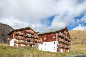 Ein Chalet-ähnliches Gebäude aus Holz mit mehreren Balkonen vor einer Bergkulisse.