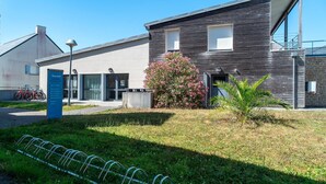 Un bâtiment moderne, avec une enseigne, un porte-vélos et un petit arbre.