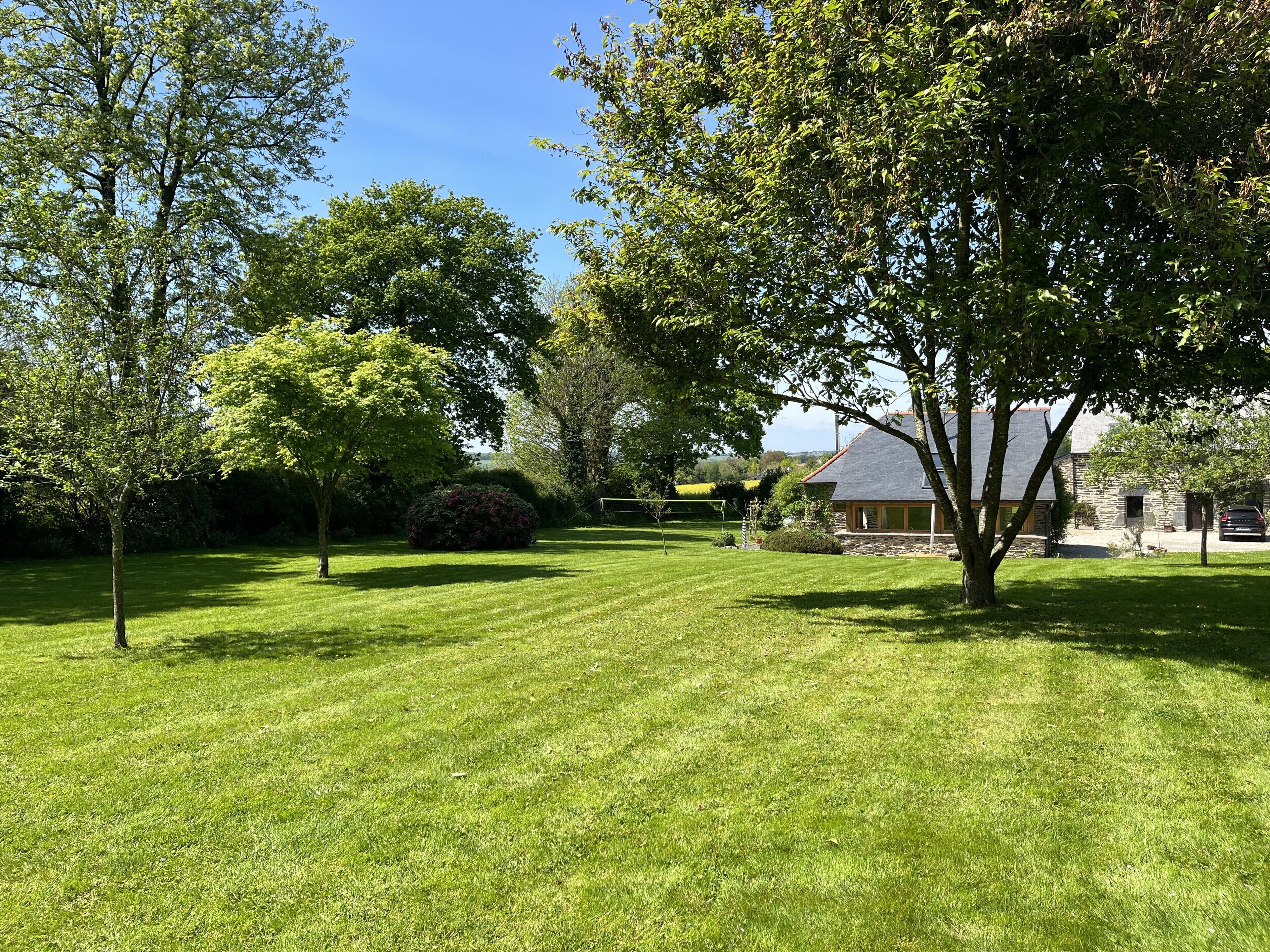 Une pelouse bien entretenue, un bâtiment en pierre et une variété d’arbres.