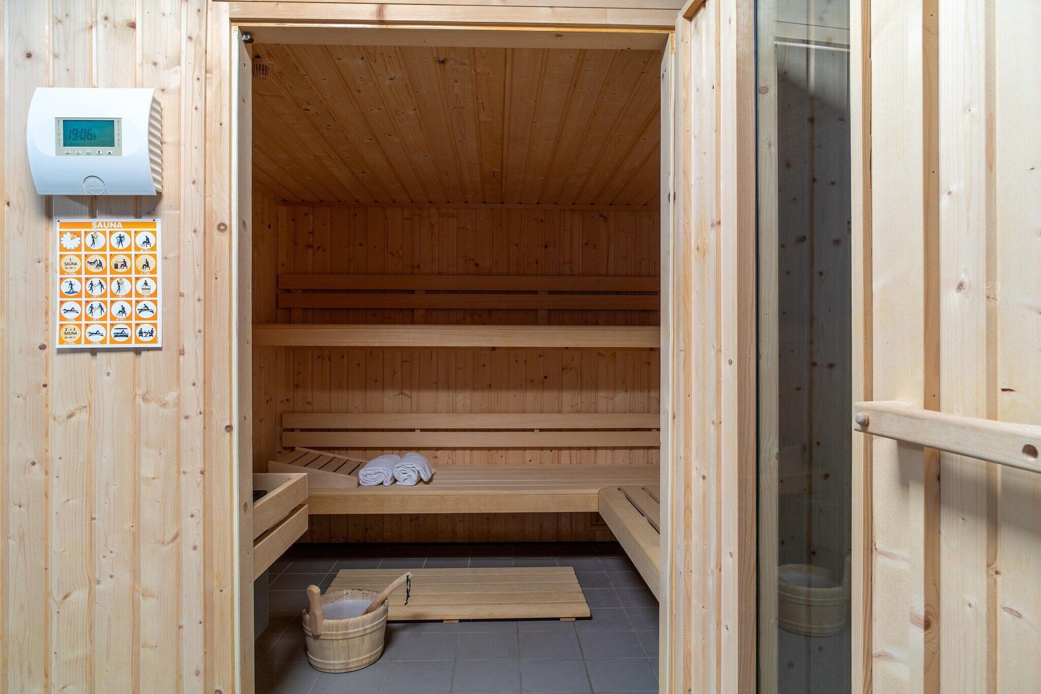 A sauna with wooden benches, a control panel, and a wooden floor.