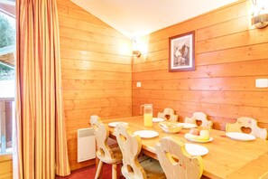 Ein Zimmer mit Holzvertäfelung, einem für vier Personen gedeckten Esstisch, einem Saftkrug und stuhlformigen Herzchen.
