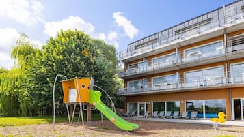A modern building with a balcony, a playground with a slide, and a pool area.