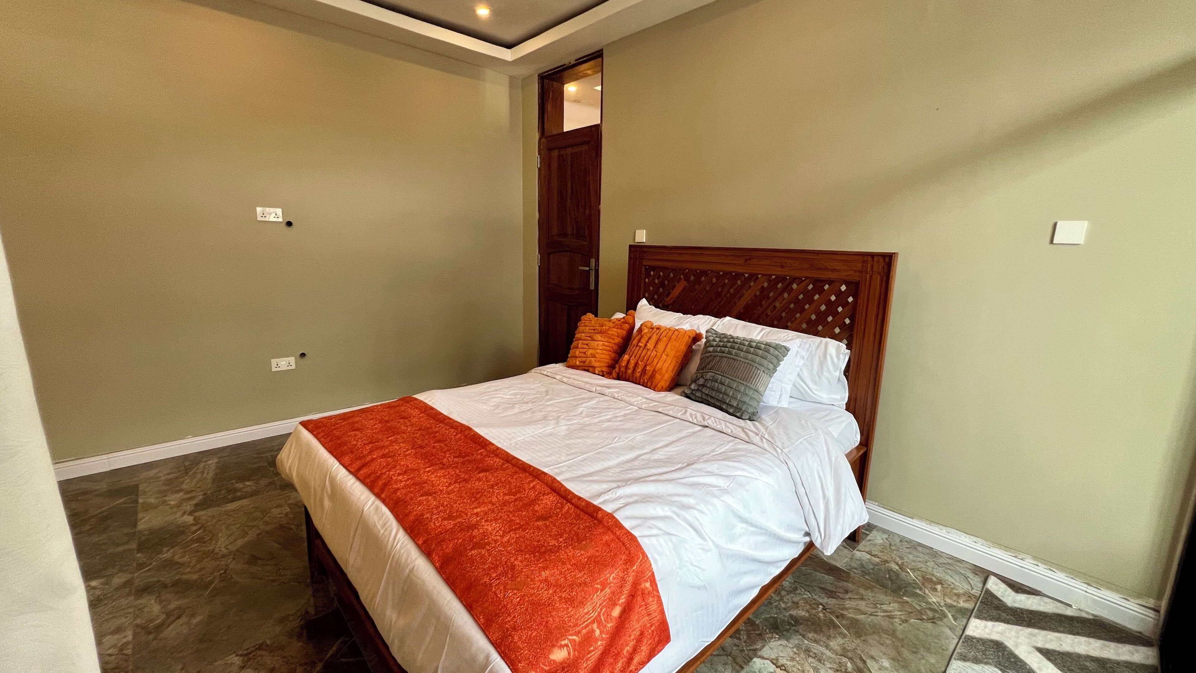 A bedroom with a bed, a wooden headboard, a red blanket, and a marble floor.