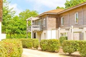 Un bâtiment en bois à deux étages, doté d’un balcon et entouré de haies bien entretenues.