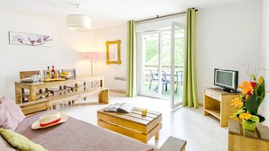 Ein modernes Wohnzimmer mit einer Couch, einem Couchtisch und einem Esstisch. Ein Fernseher steht auf einem Schrank und es gibt ein Fenster mit Vorhängen.