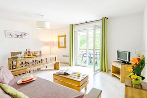 Ein modernes Wohnzimmer mit einer Couch, einem Couchtisch und einem Esstisch. Ein Fernseher steht auf einem Schrank und es gibt ein Fenster mit Vorhängen.