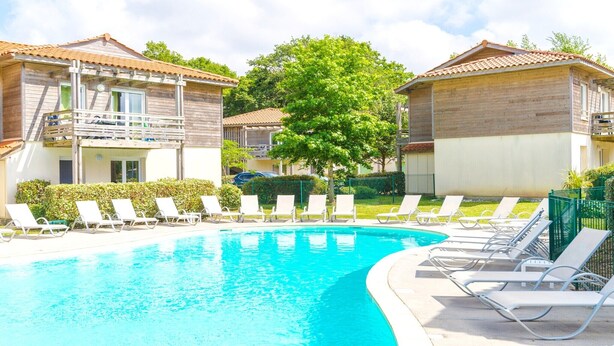 Ein Swimmingpool mit Liegestühlen, einem Baum und zwei Gebäuden mit Balkonen.