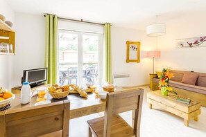 Una habitació ben il·luminada amb una taula de dinar preparada per l'esmorzar, un sofà i una televisió.