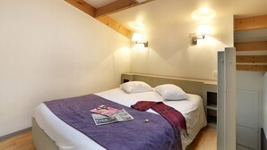 Un dormitorio con tragaluz, dos lámparas de pared, una cama con manta morada y una revista.