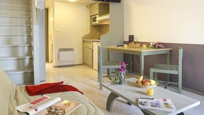 Ein gemütliches Wohnzimmer mit einer Couch, einem Couchtisch mit Zeitschriften, einem an der Wand montierten Fernseher und einer Treppe, die in eine obere Ebene führt.