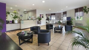 Vestíbulo de hotel con mostrador de recepción, zona de estar y cocina al fondo.
