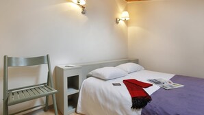 Un dormitorio con una cama, una mesita de noche, una silla y dos lámparas de pared.