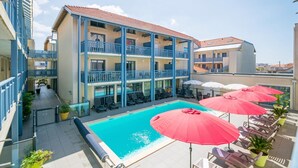 Ein Hotel mit Schwimmbad, Balkonen und Sitzgelegenheiten im Freien mit Sonnenschirmen.
