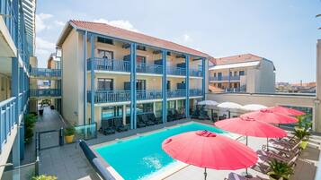 Un hôtel doté d’une piscine, de balcons et d’un espace extérieur aménagé avec des parasols.