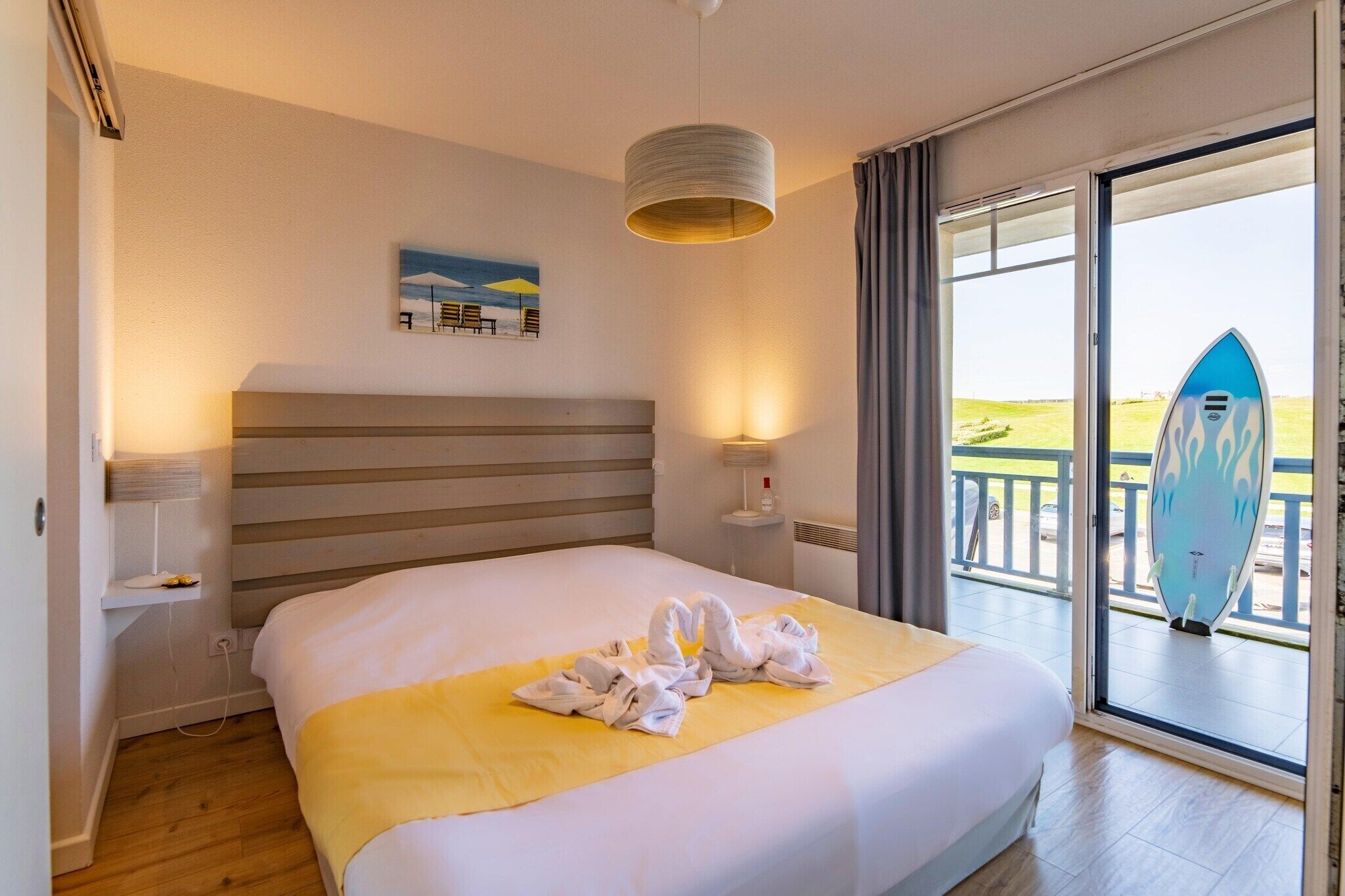 Habitación de hotel con cama, un cuadro, una lámpara, una ventana con vistas y una tabla de surf.