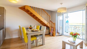 Un comedor con una escalera de madera, una mesa de comedor con sillas, una mesita con un florero y vistas a través de un ventanal.