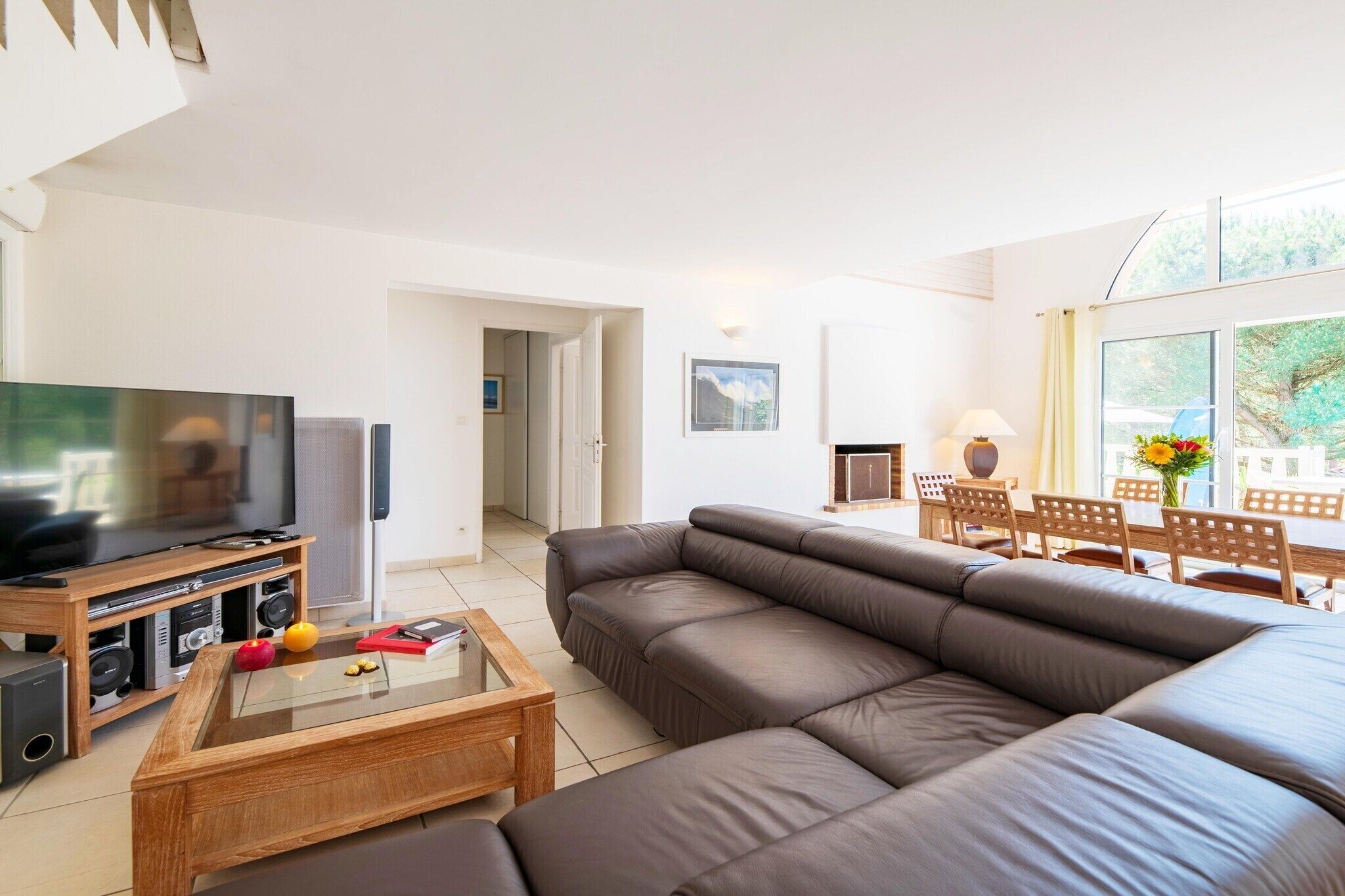 A modern living room with a flat-screen TV, a leather sofa, a wooden coffee table, and a dining area with a table and chairs.
