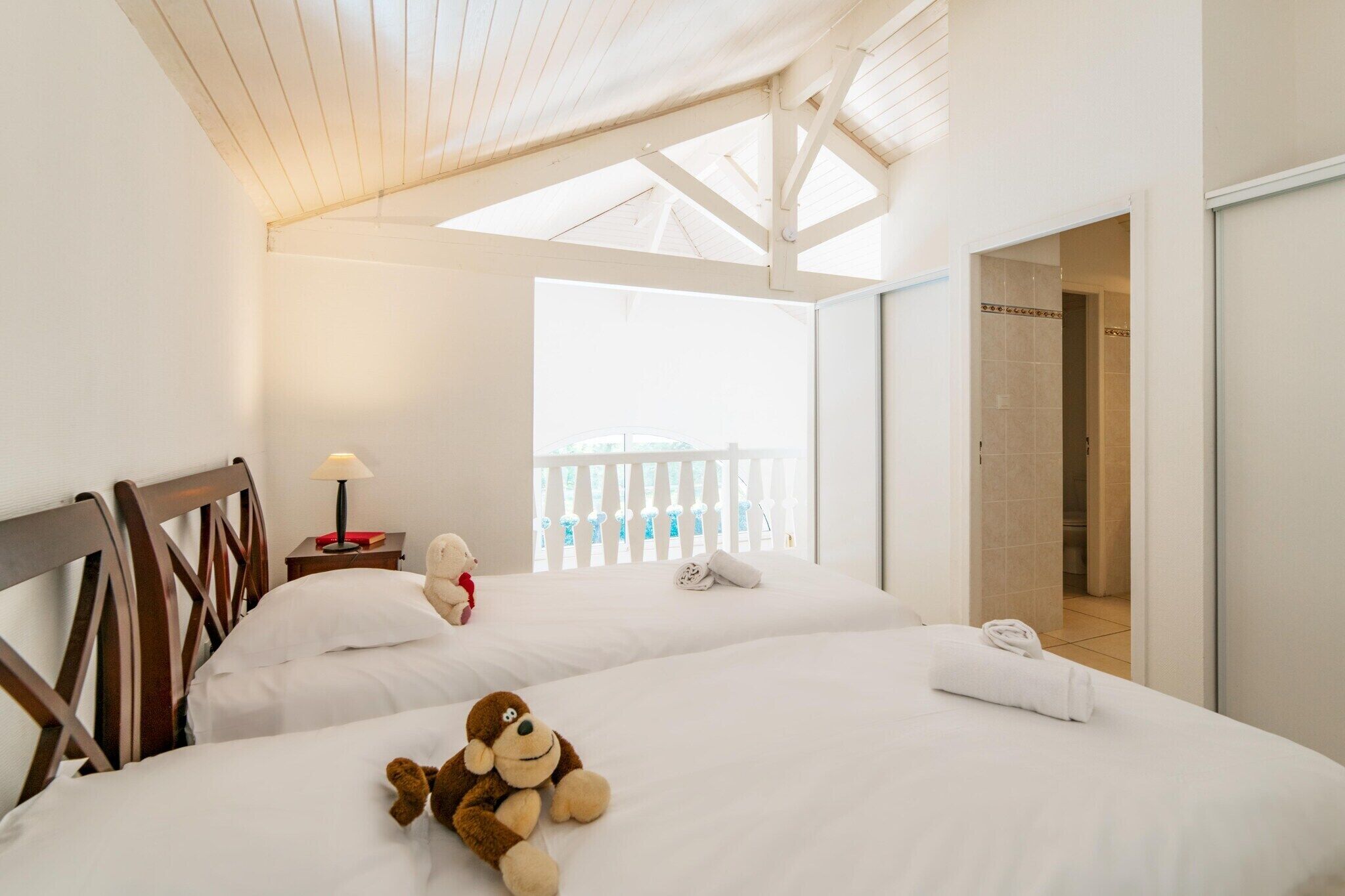 Une chambre d’hôtel avec deux lits, un plafond en bois, un balcon doté d’une balustrade blanche et un espace douche.