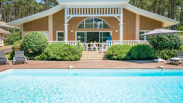Ein Poolbereich mit Holzterrasse, einer überdachten Veranda und Blick auf eine bewaldete Landschaft.