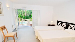 Ein Schlafzimmer mit zwei Betten, einem Sessel, einem Nachttisch und einem Balkon mit weißer Brüstung.