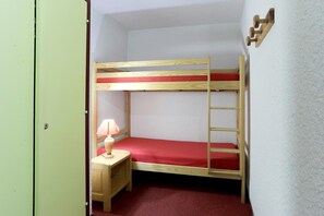 Une chambre avec un lit superposé, une échelle en bois, une petite table de chevet avec une lampe et un matelas rouge.