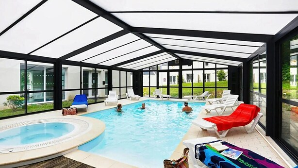 Une piscine intérieure entourée de baies vitrées, avec des chaises longues et un jacuzzi.