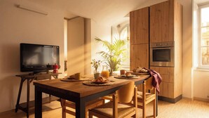 A dining area with a wooden table, chairs, a television, and a kitchen with wooden cabinets and appliances. - Edward Historic House (Gubbio)