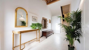 A hallway with a gold-framed mirror, a console table with a plant, a dark wooden cabinet, and a large potted plant. - Edward Historic House (Gubbio)