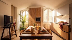 A modern kitchen with wooden cabinets, a dining table set with bread, a TV, and a plant. - Edward Historic House (Gubbio)