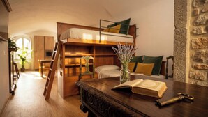 A cozy room with a bunk bed, a wooden desk with an open book, a vase with flowers, and a stone wall. - Edward Historic House (Gubbio)