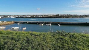 A coastal view with boats docked at a pier, a stone breakwater, and a distant town. - Spacious Coastal Duplex Cottage for 8 (Audierne)