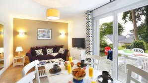 A modern living room with a sofa, television, and dining area with breakfast items. - Spacious Coastal Duplex Cottage for 8 (Audierne)